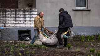 Коммунальщики несут в ковре тело мужчины, похороненного в своем дворе в Гостомеле Киевской области.